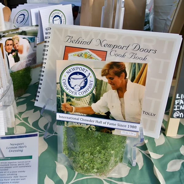 A cookbook, Newport Chowder Company branding, and a bag of dried herbs on a green patterned tablecloth.