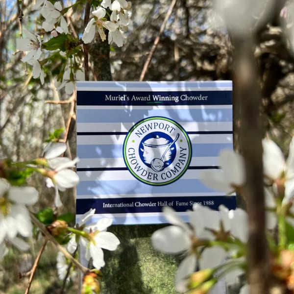 A Newport Chowder Company award sign, "Muriel's Award Winning Chowder," surrounded by white blossoms.