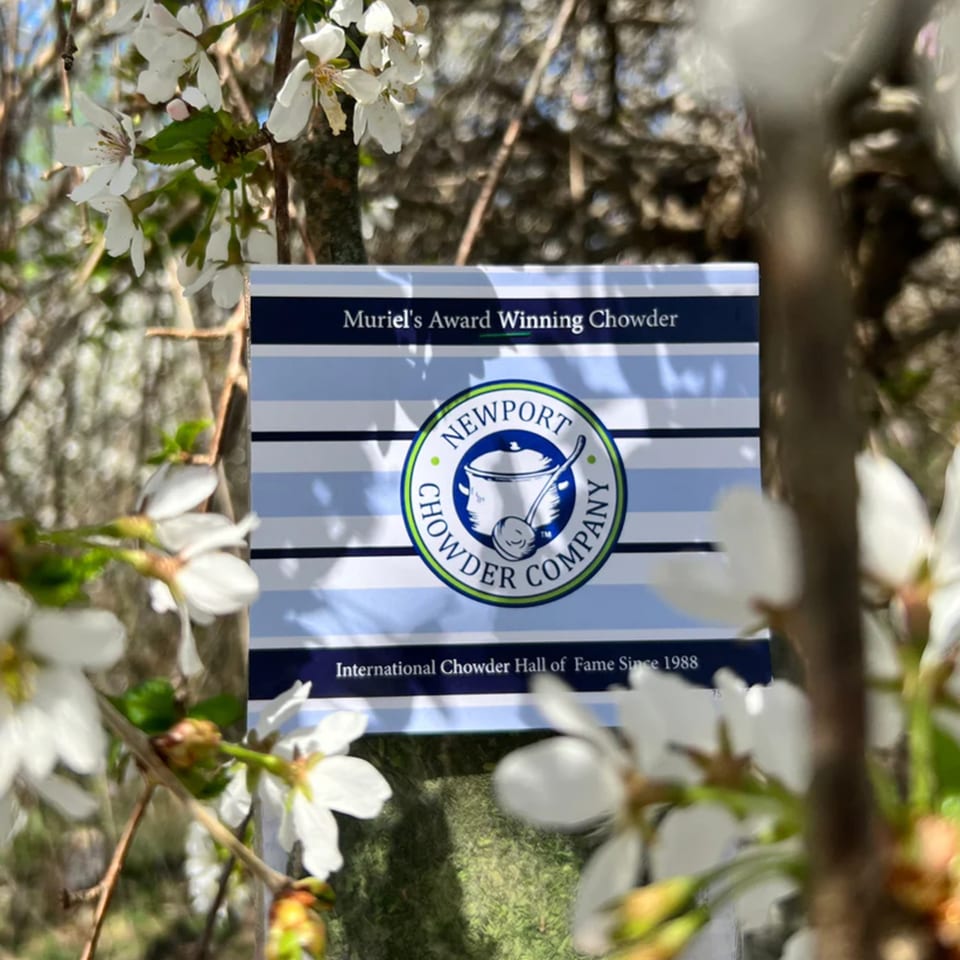 A Newport Chowder Company award sign, "Muriel's Award Winning Chowder," surrounded by white blossoms.