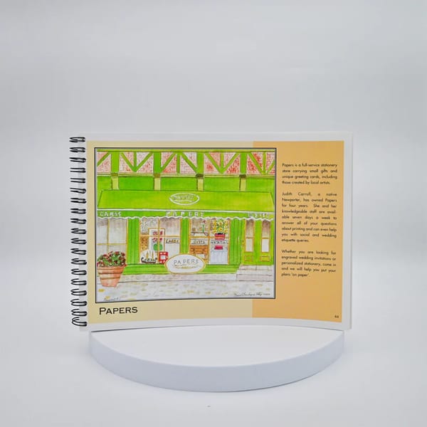 A spiral-bound book open to a page with a colorful illustration of a storefront named "Papers" and descriptive text.