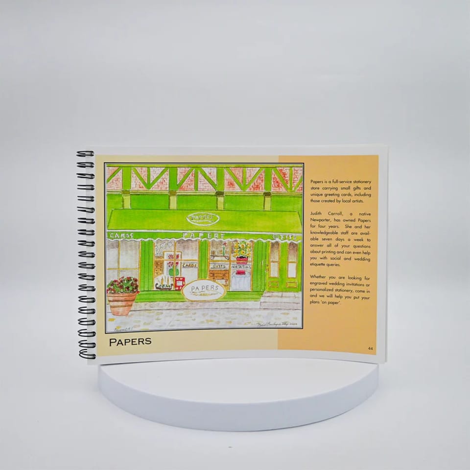 A spiral-bound book open to a page with a colorful illustration of a storefront named "Papers" and descriptive text.