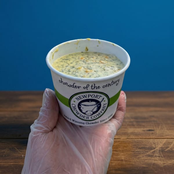 A gloved hand holds a cup of Newport Chowder Company's creamy chowder with herbs and vegetables.