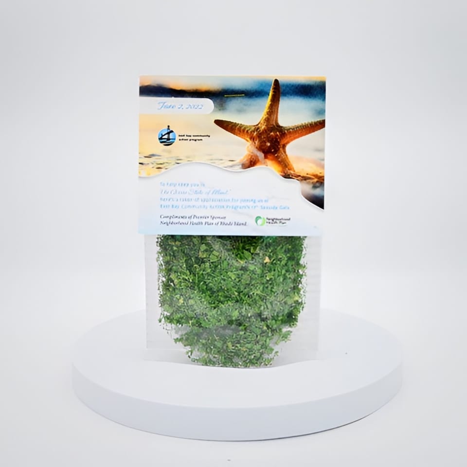 A clear plastic bag filled with green leafy herbs, topped with a beach-themed label featuring a starfish.