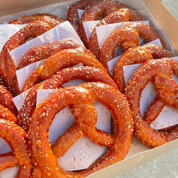 A box filled with many golden-brown, salted pretzels, each separated by white parchment paper.