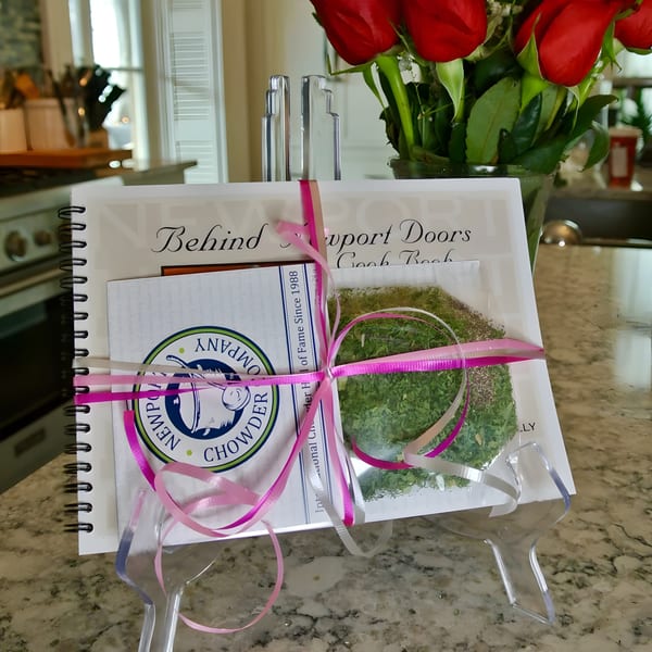 A cookbook and chowder mix, tied with pink ribbons, displayed on a kitchen counter with red roses.